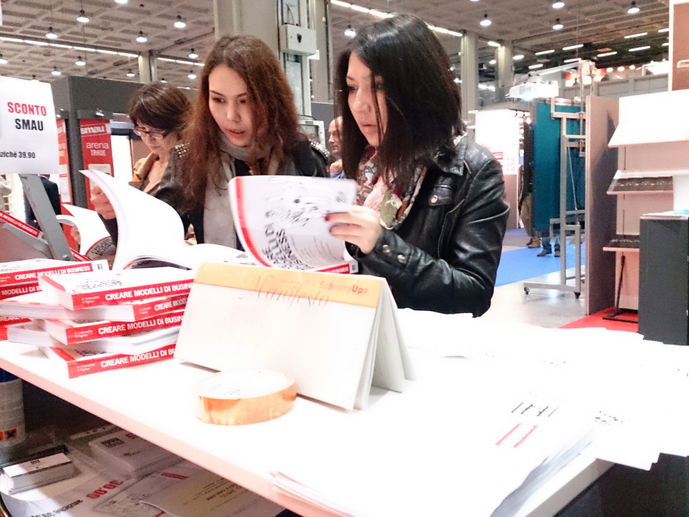 Delle ragazze sfogliano una copia di 'Creare modelli di business' allo stand dell'editore FAG allo SMAU Milano.
