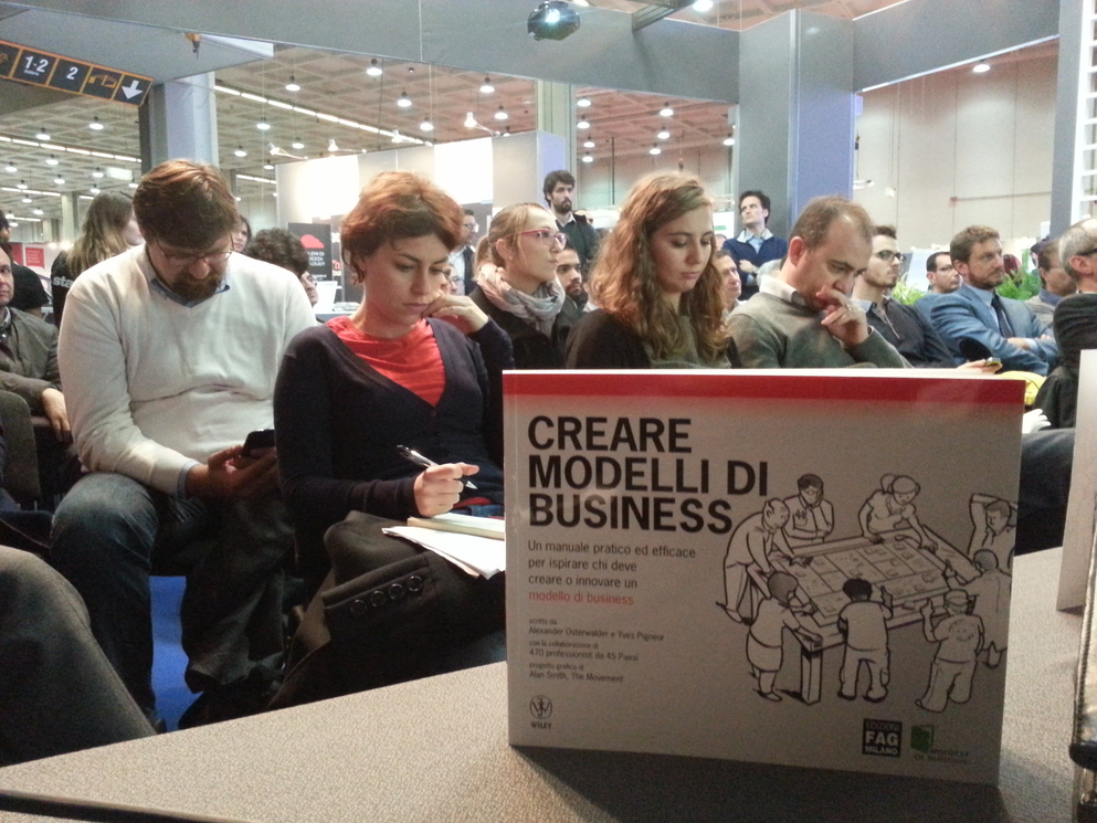 Fotografia della copertina del libro 'Creare Modelli di Business' in primo piano, con il pubblico sullo sfondo.